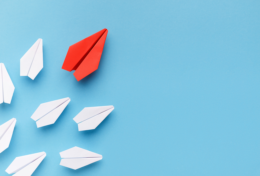 Red paper plane leading white ones on blue background.