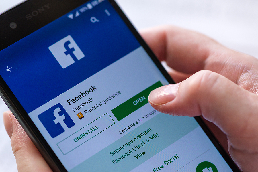 A person's thumb installing the Facebook app on their cellphone despite the Facebook advertising boycott