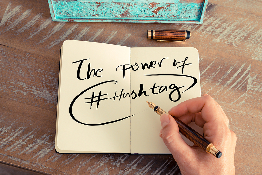"The Power of #Hashtag" written in an open notebook underneath a woman's hand holding a pen.