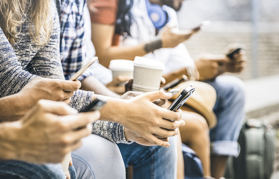 A group of people sitting on a bench using their cellphones, representing new social media trends