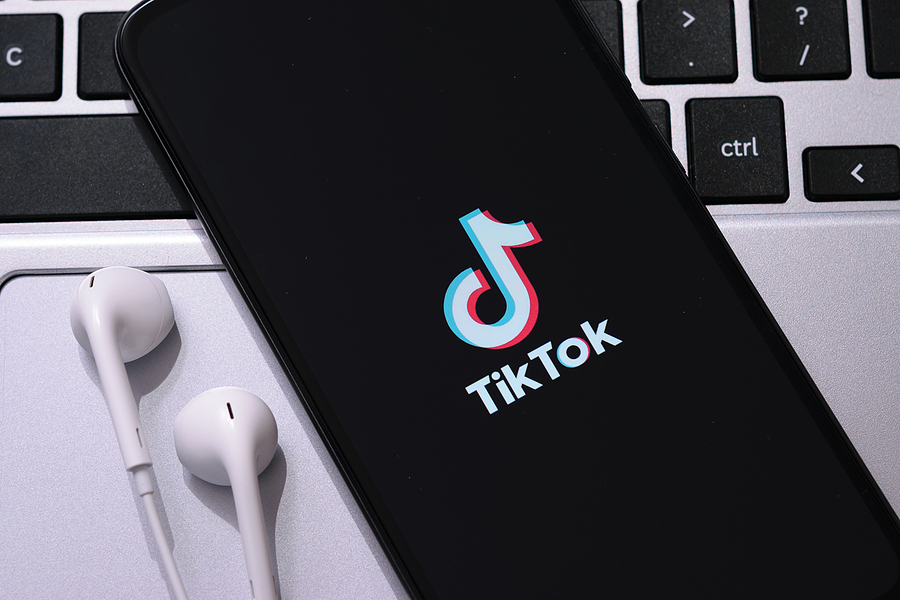 A cellphone with earbuds sitting atop a laptop keyboard with the TikTok app displayed on the screen.