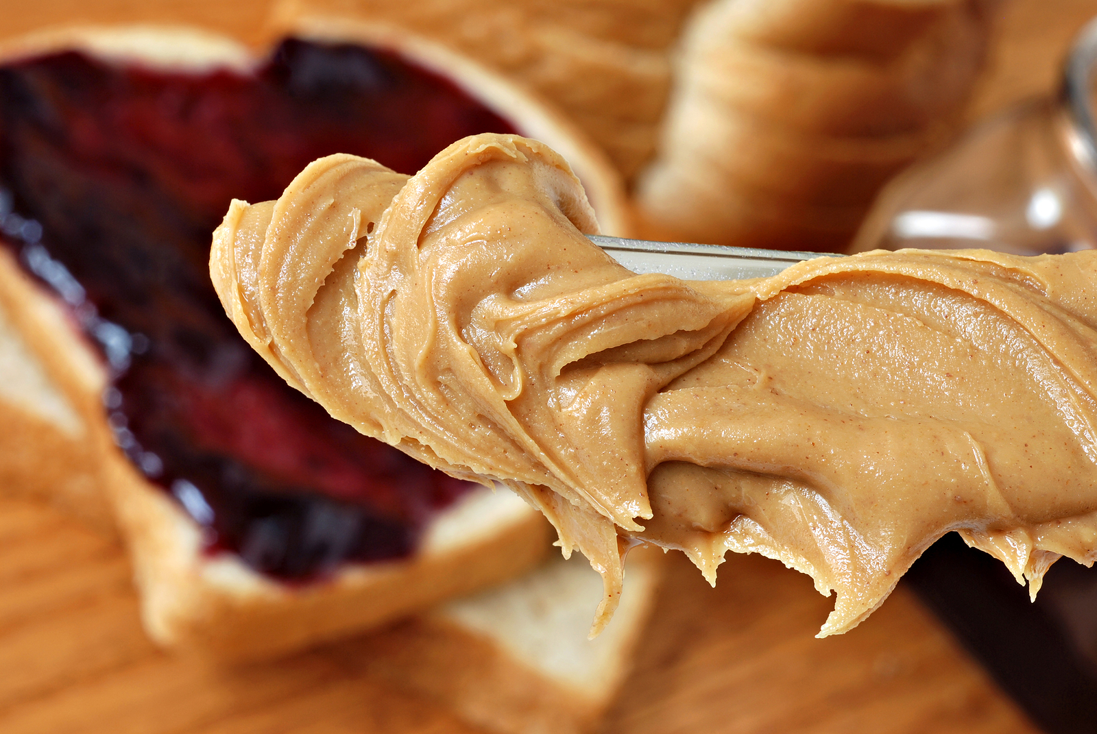 Peanut butter on a butter knife above a slice of bread with jam.