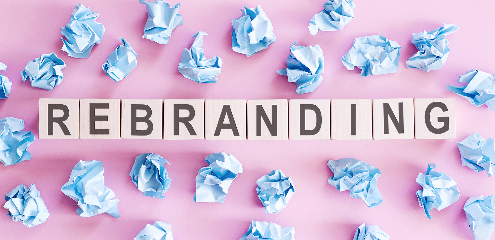 Rebranding written on white blocks on a pink background with crumpled balls of blue paper.