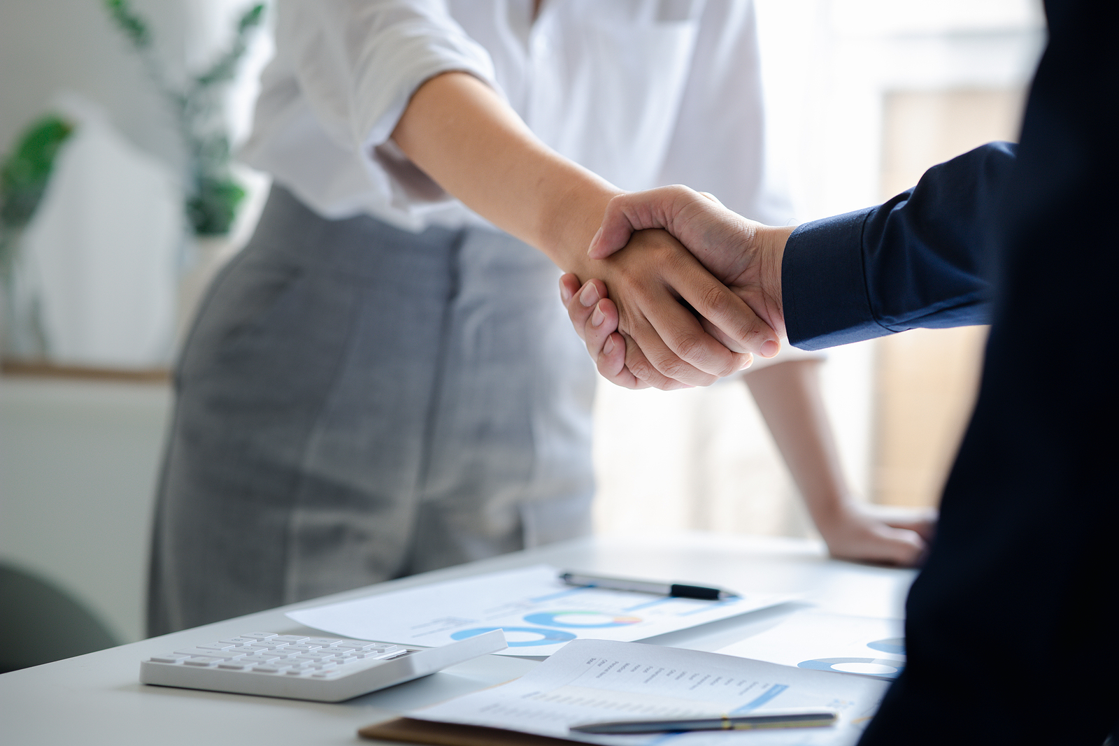 Businessman and businesswoman shaking hands over office table.