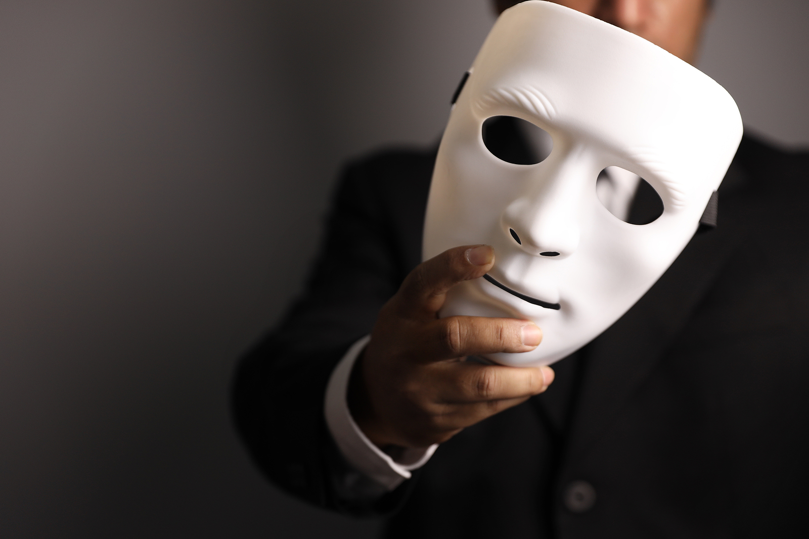 Businessman in suit holding a featureless white mask up to their face.